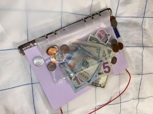 A notebook with a clear plastic top cover with a collection of paper and coin money tucked inside.