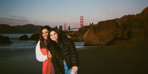 Two college women are standing outside with the Golden Gate Bridge behind them.
