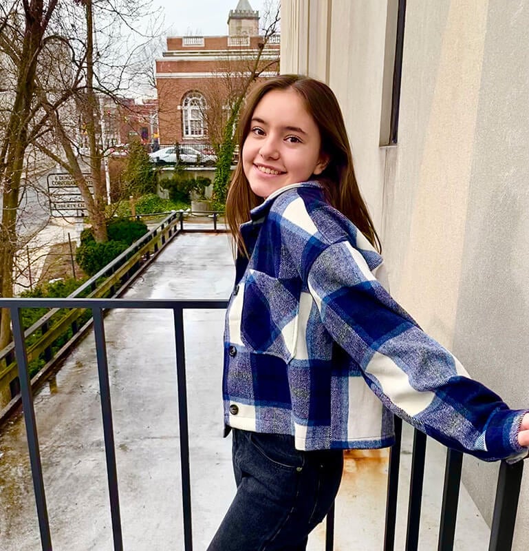 Blog author Maddy Beavis stands on a ramp outside on her college campus. She is wearing blue and white checkered jacket and is holding the railing behind her. 