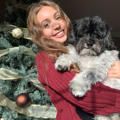 Blog author Maria Lutz is holding a small black and white dog in front of a Christmas tree. 