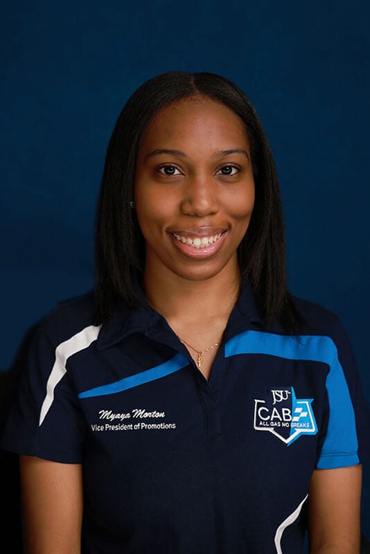 A studio headshot of blog author Myaya. She has medium length dark straight hair, and is wearing a blue polo shirt with the Campus Activities Board logo on the pocket area.