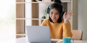 Student waving at a laptop while wearing headphones.  