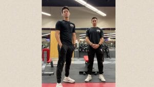 Two male college students stand in front of weight room equipment. They are both wearing black sweat pants and black t-shirts with UNLV pocket logos.
