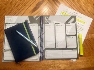An overhead view of a student’s desk featuring an open student planner, a closed notebook, and pen.