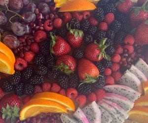 An arrangement of colorful fruit featuring red grapes, pomegranate seeds, raspberries, black berries, strawberries, star fruit, and orange slices.
