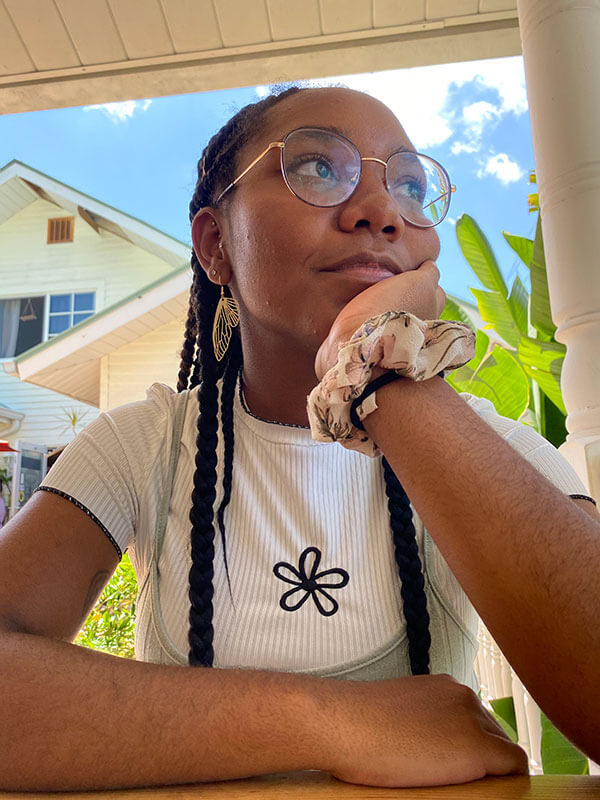 Blog author Rachel Stennett is sitting at a table with her chin leaning on one hand. She is a white t-shirt with a small flower on the front and is also wearing glasses and looking off to her left.