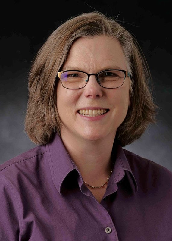 Blog author Ruth Heisler has medium length brown hair and glasses, and is wearing a purple blouse.