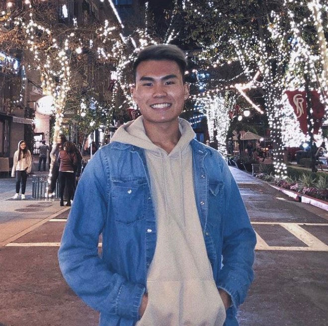 Blog author Stephen Chau is standing in a street lined with trees decorated with white lights. He is smiling and wearing a blue denim jacket.