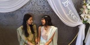 Two young Indian women looking at each other and smiling. They are wearing traditional Indian saris.