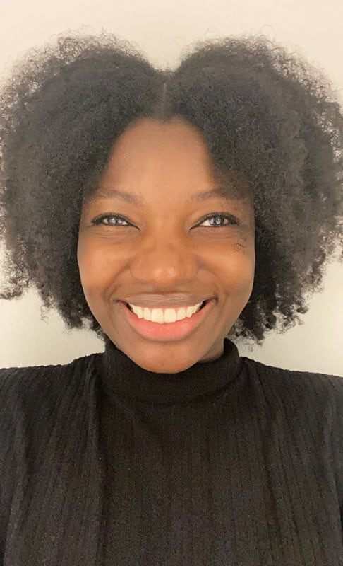 Blog author Stella Seth is smiling and wearing a dark turtle neck top and jacket. She has dark curly hair parted in the middle.
