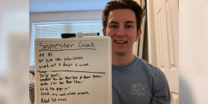Blog author Tommy is wearing a blue t-shirt and holding up a small dry erase board, on which he has written out his weekly goals.