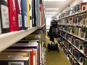 Two tall library bookshelves with an empty electric wheelchair in the aisle between the shelves.