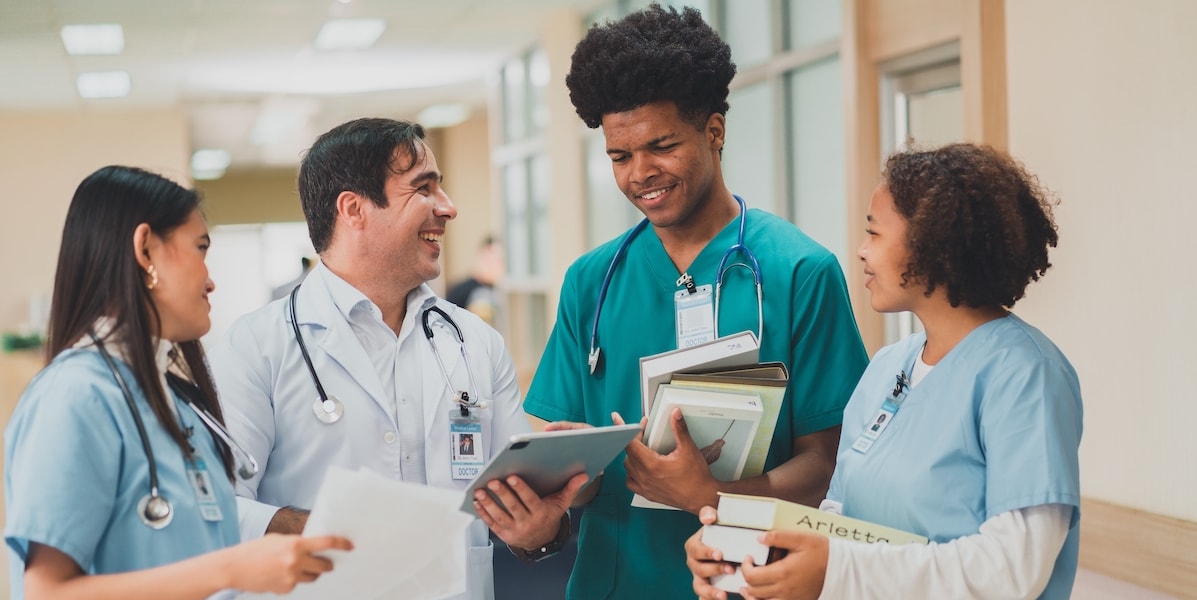 Three nursing students and a doctor smiling while looking at the doctor's tablet.