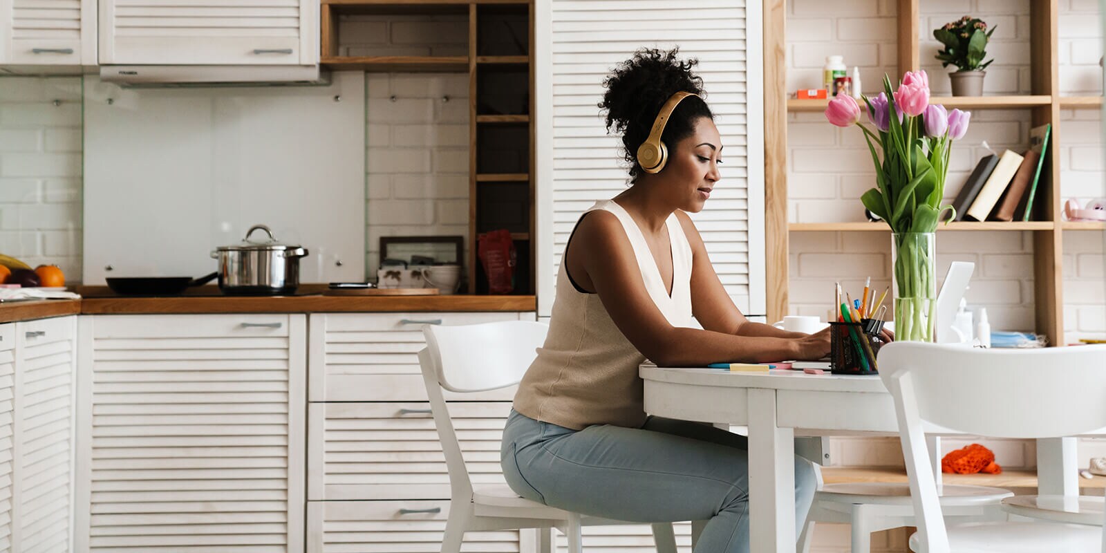 A woman sitting at a table and working on laptop with headphones on.