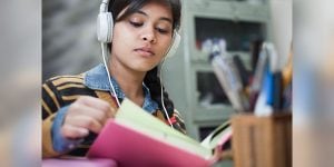 A female college student reads a book and listens to music with headphones