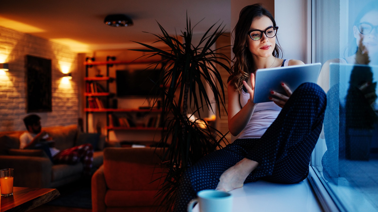 Female student sitting on window ledge reviewing content on mobile device