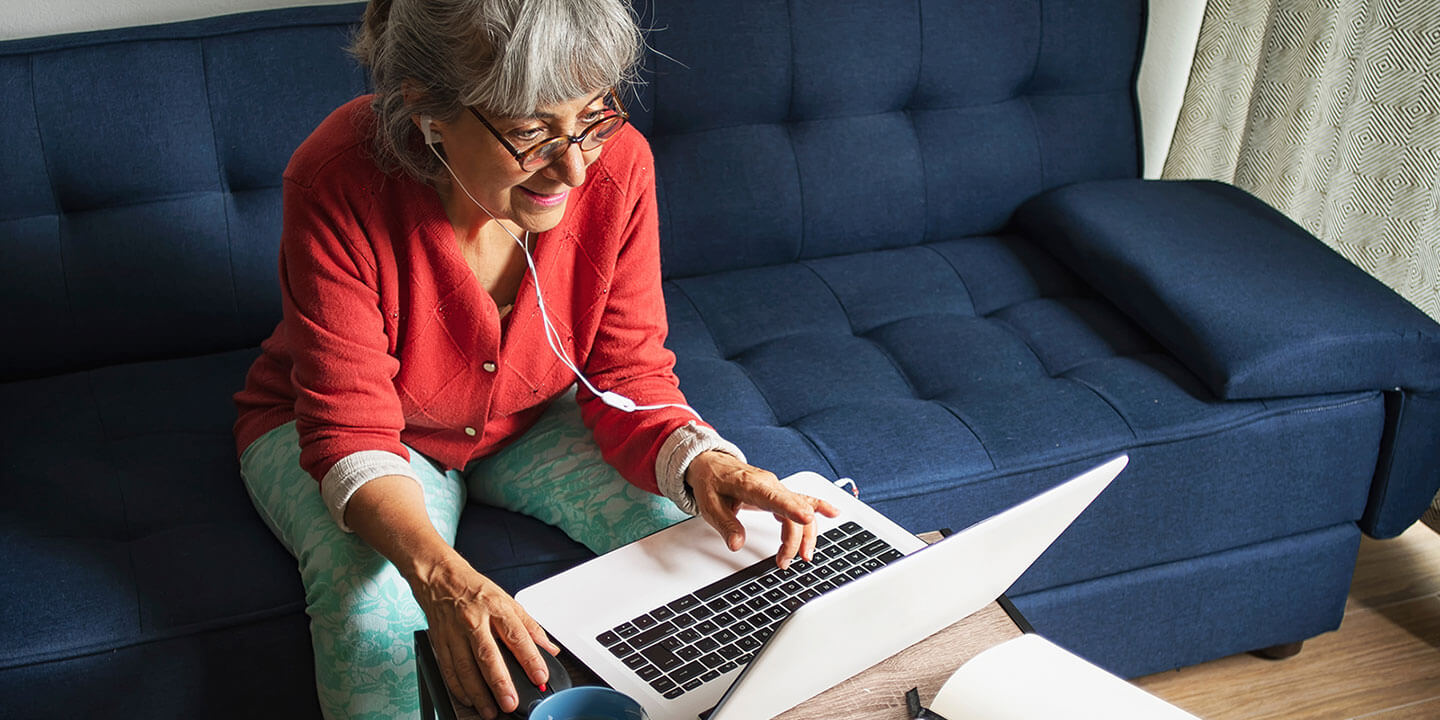 A woman working on a computer sitting on a couch with ear phones on