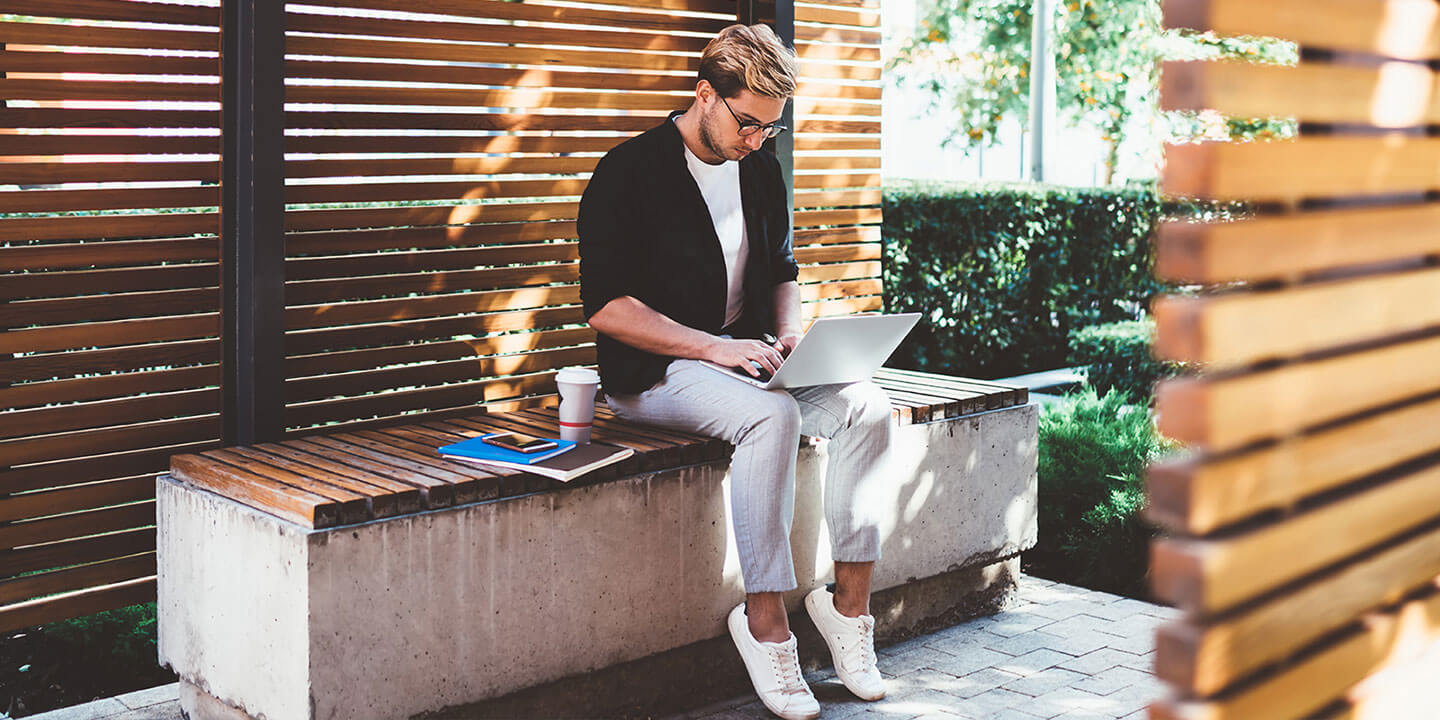 A man working on computer sitting on a bench.