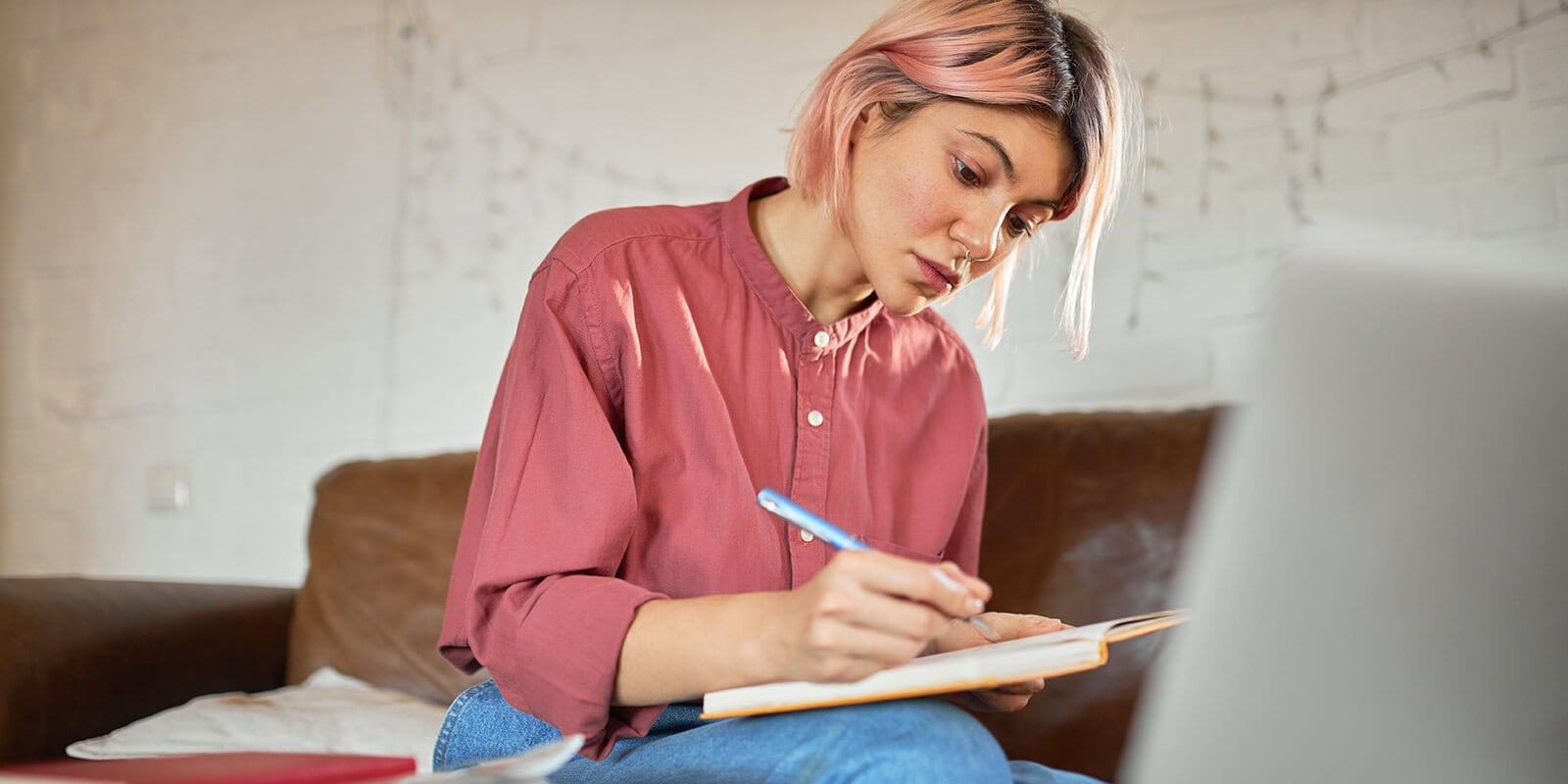 A woman taking notes in a notebook infront of laptop