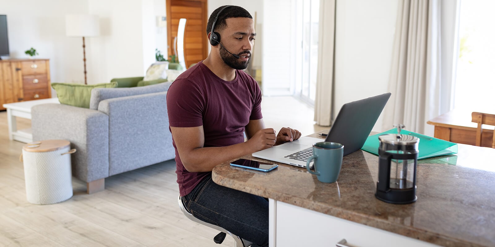 A man working sitting at the kitchen counter top and working on the laptop