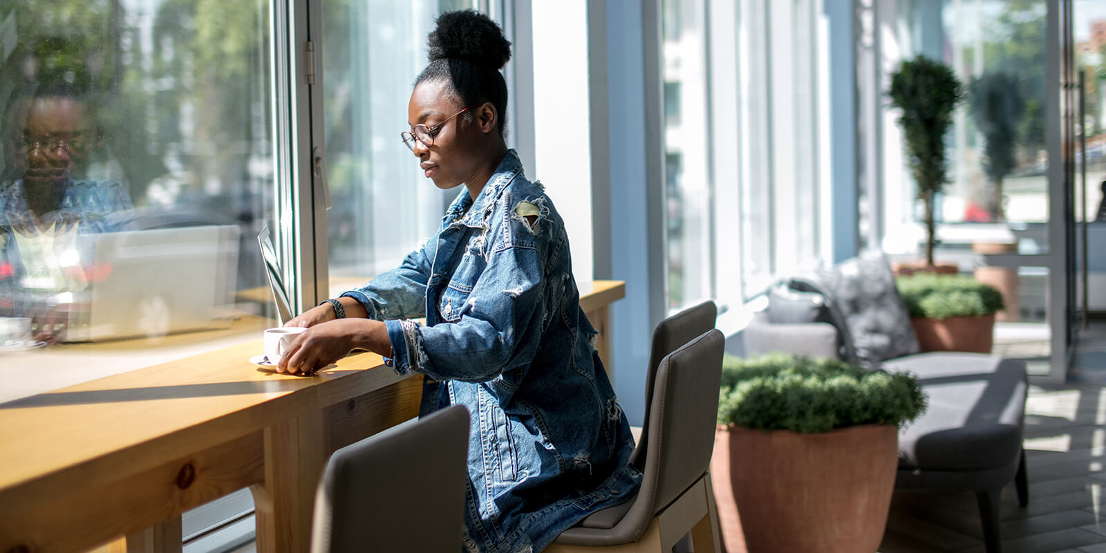 A woman sitting in chair with laptop on the desk and a cup of coffee