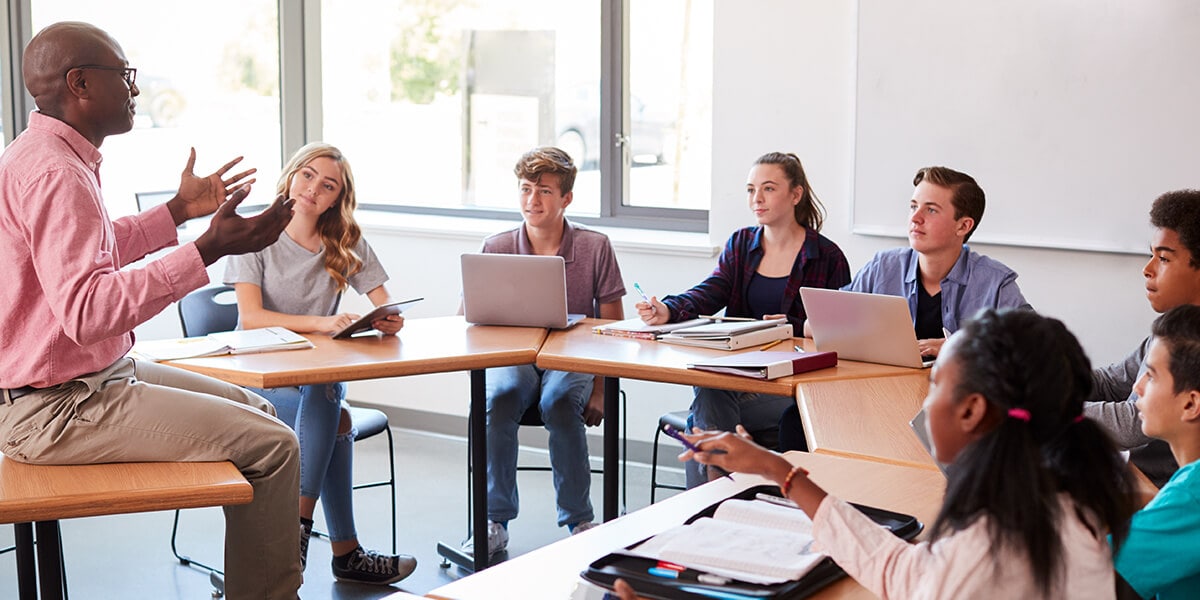 Male teacher speaking to students in a classroom. 