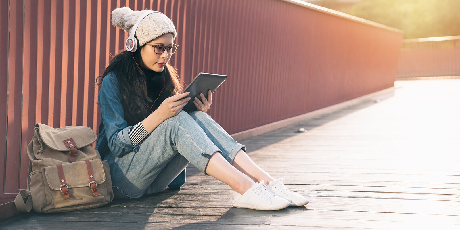 Student sitting in front of corrugated wall, viewing content on their mobile device