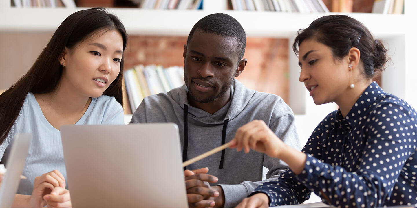 Three students are looking at a laptop screen and discussing the contents.