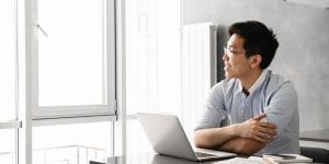 Man looking out the window, with laptop open in front of him