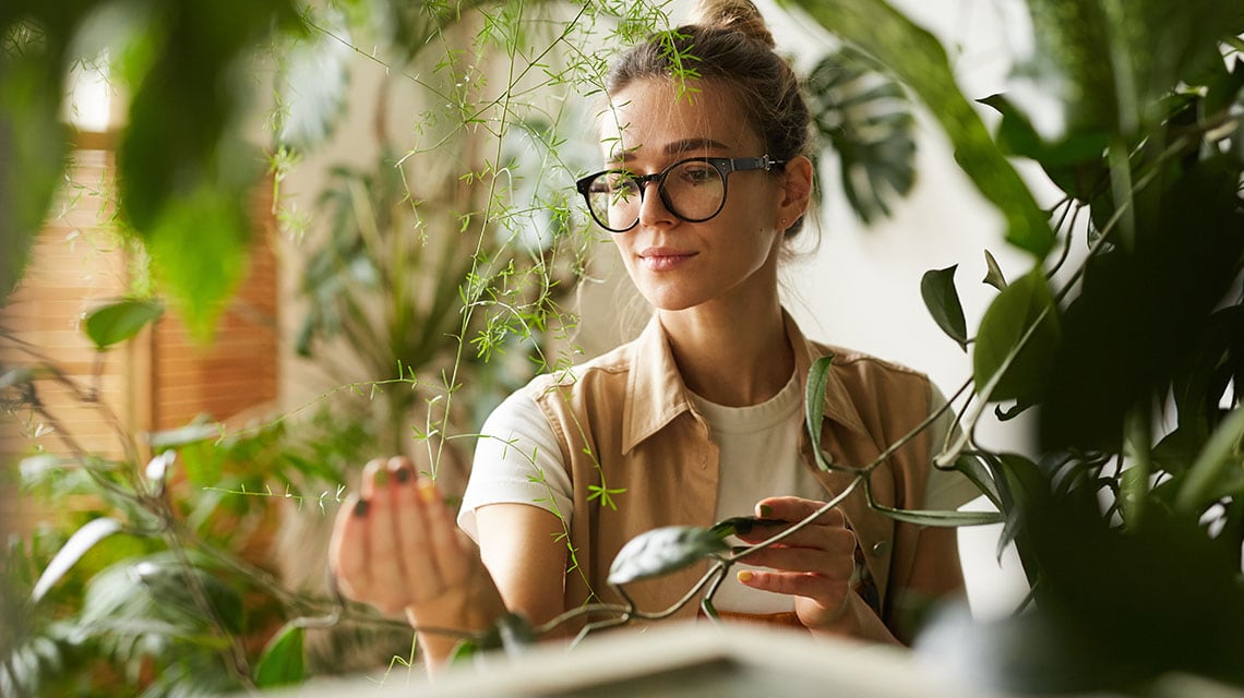 woman surrounded by plants looking at a leaf