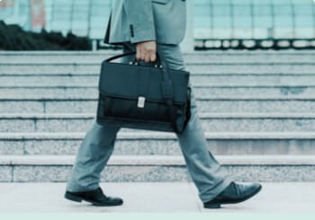 Businessman is wearing a suit and holding a briefcase, while walking outdoors alongside stairs