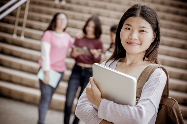 female Asian student holding a laptop