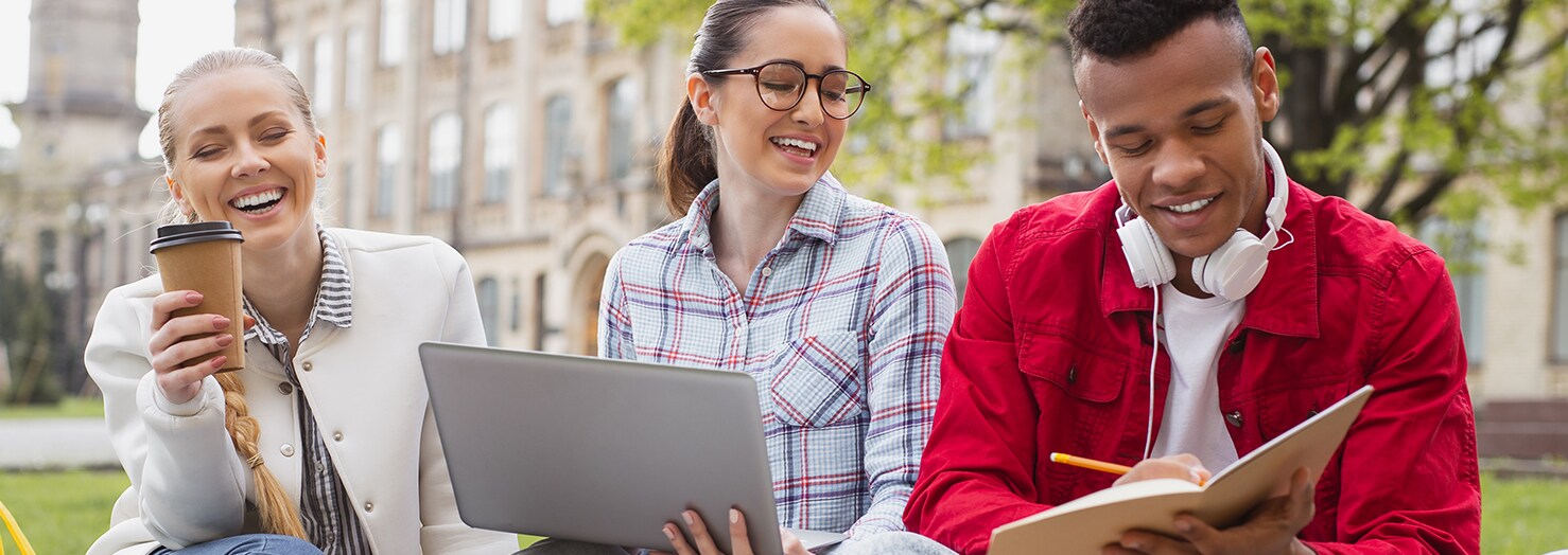 University students sitting together outside with a laptop and notepad