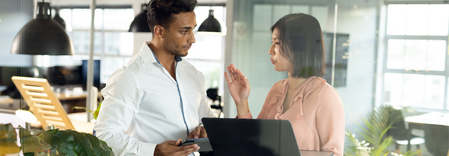 Business people stood together in a office talking to eachother, one is holding a laptop