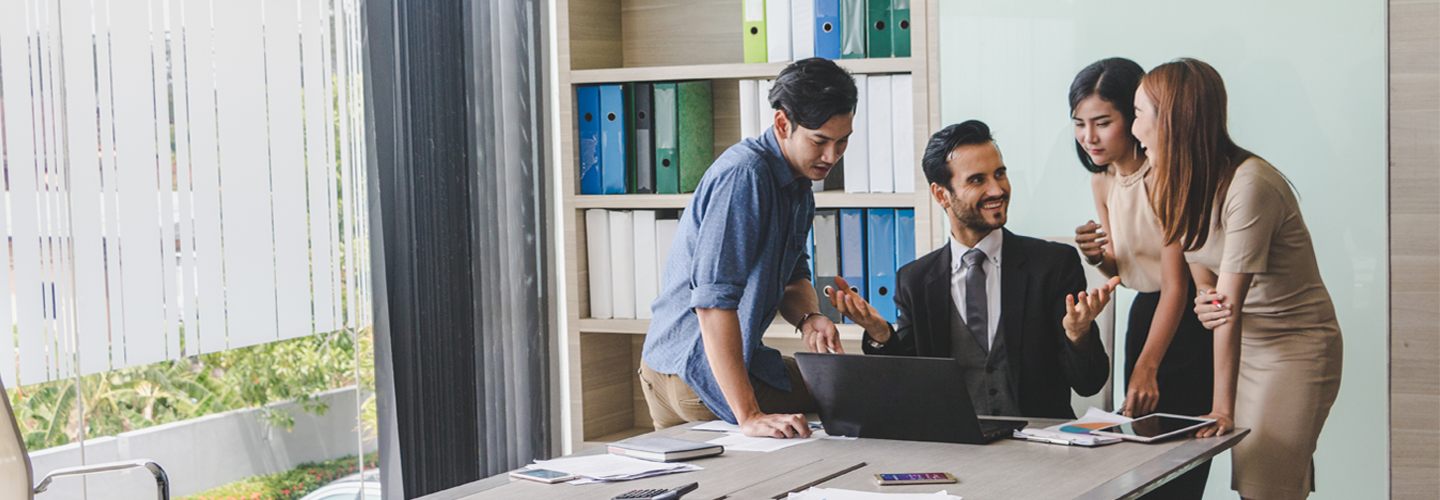 A group of busines people grouped at the end of a table in a office room chatting over a laptop
