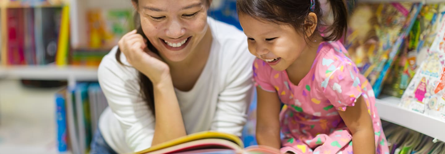 A child and a adult reading a book together in a library