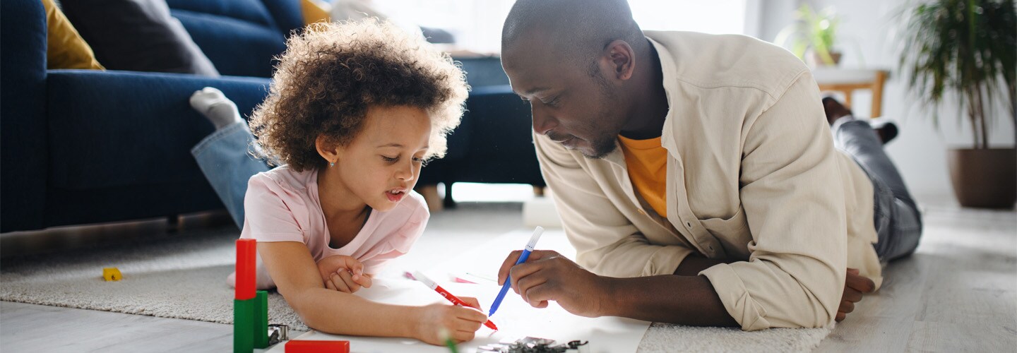 A parent and their child laying on the floor drawing together on a large peice of paper