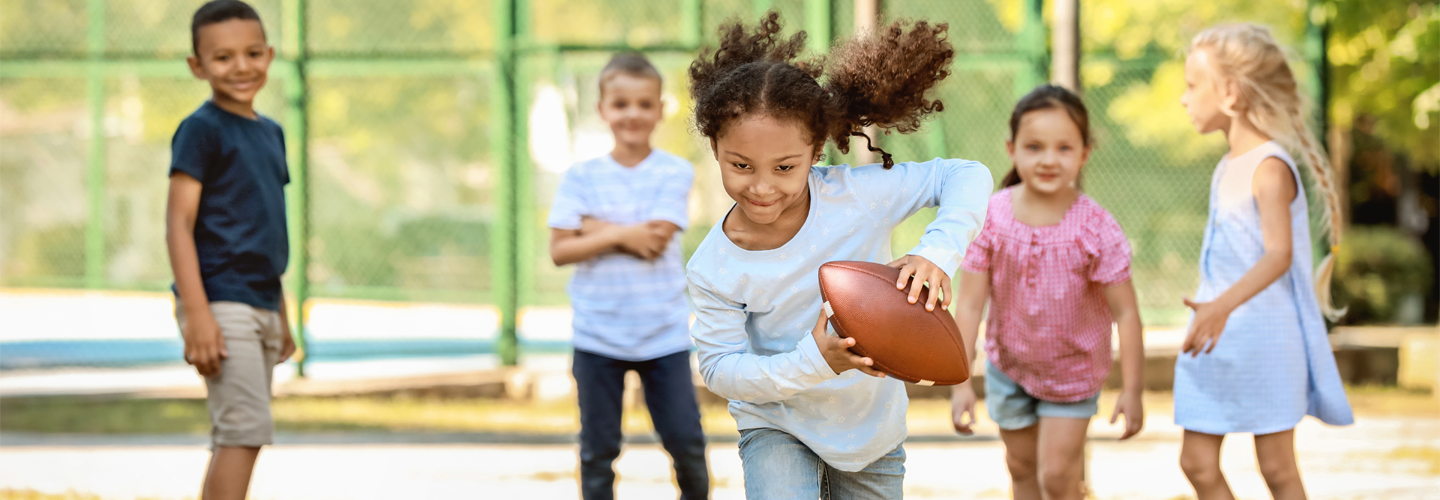 外でラグビーボールを持って走っている子供と、その後ろに子供