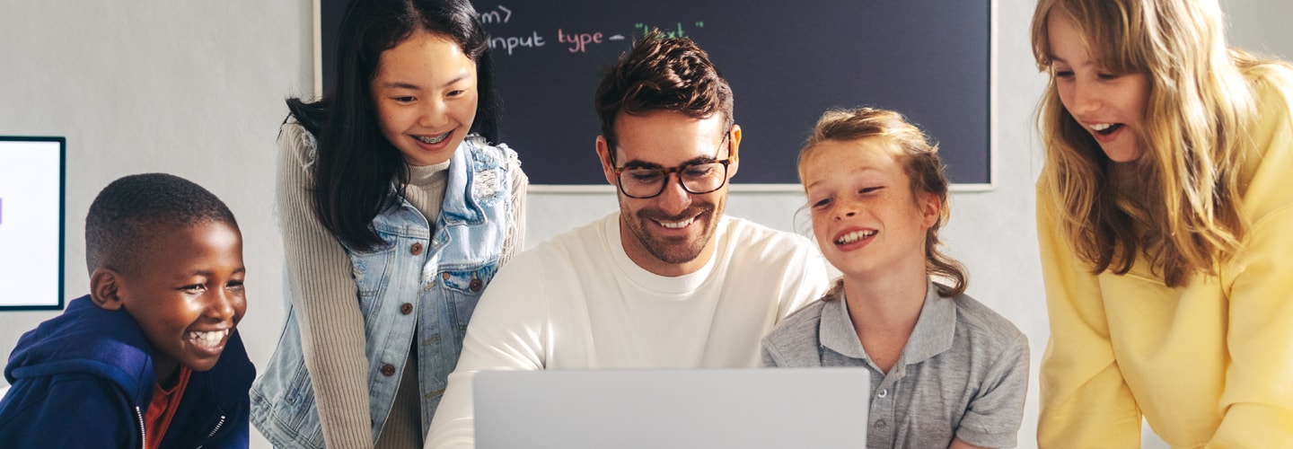 Children stood around a laptop with a teacher smiling
