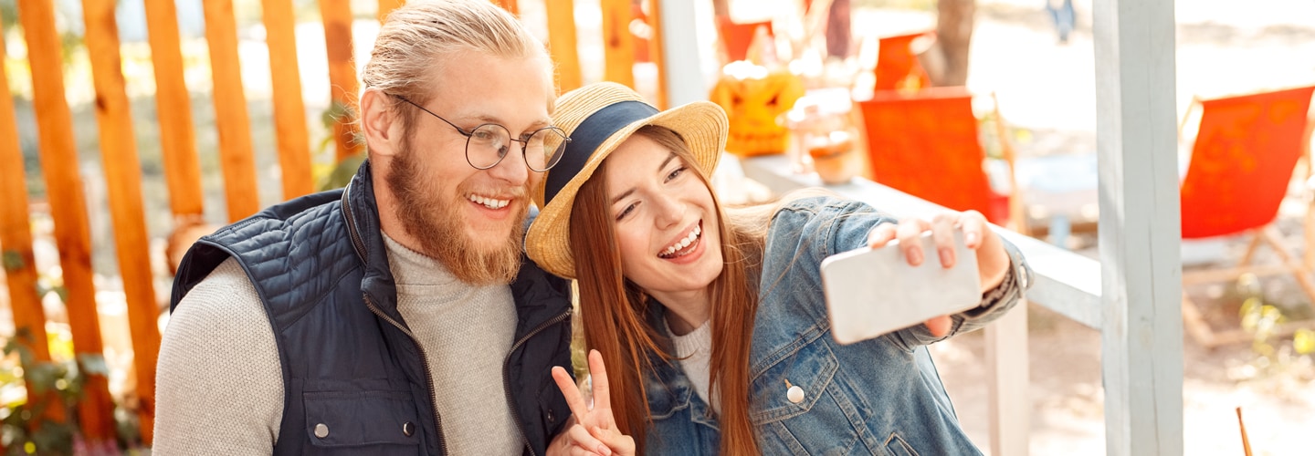 A couple smiling together taking a selfie on a phone with pumpkins in the background