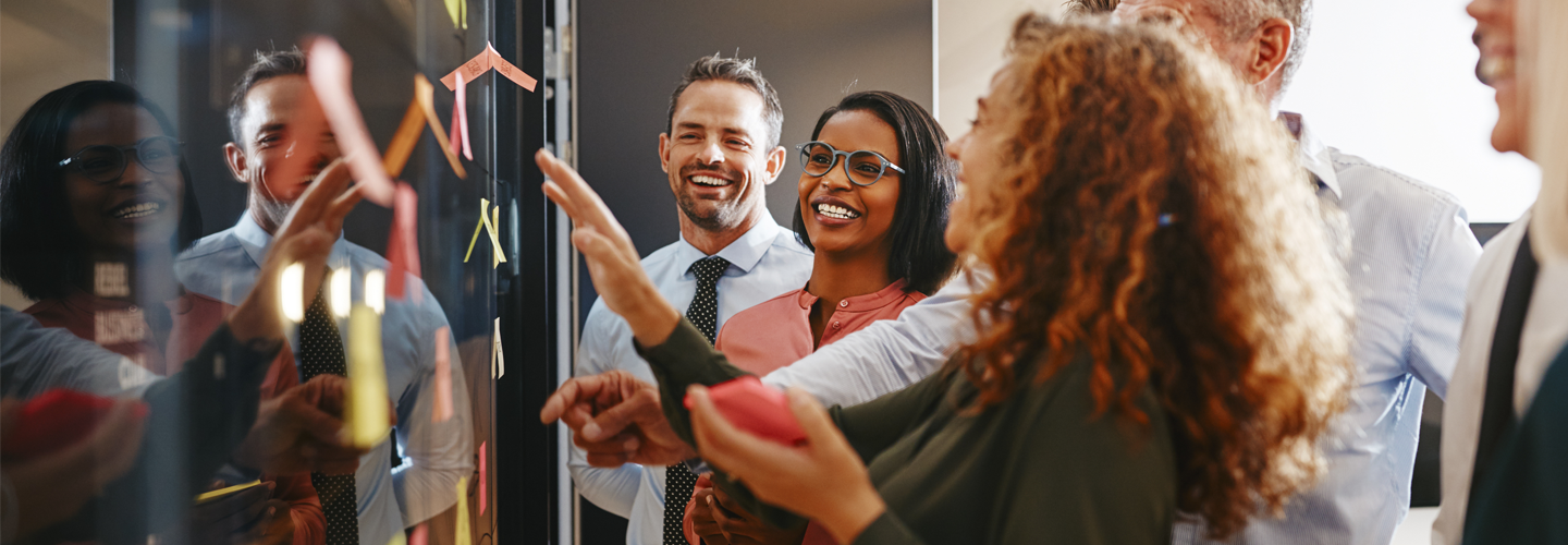 A group of business people stood around a board with sticky notes on smiling