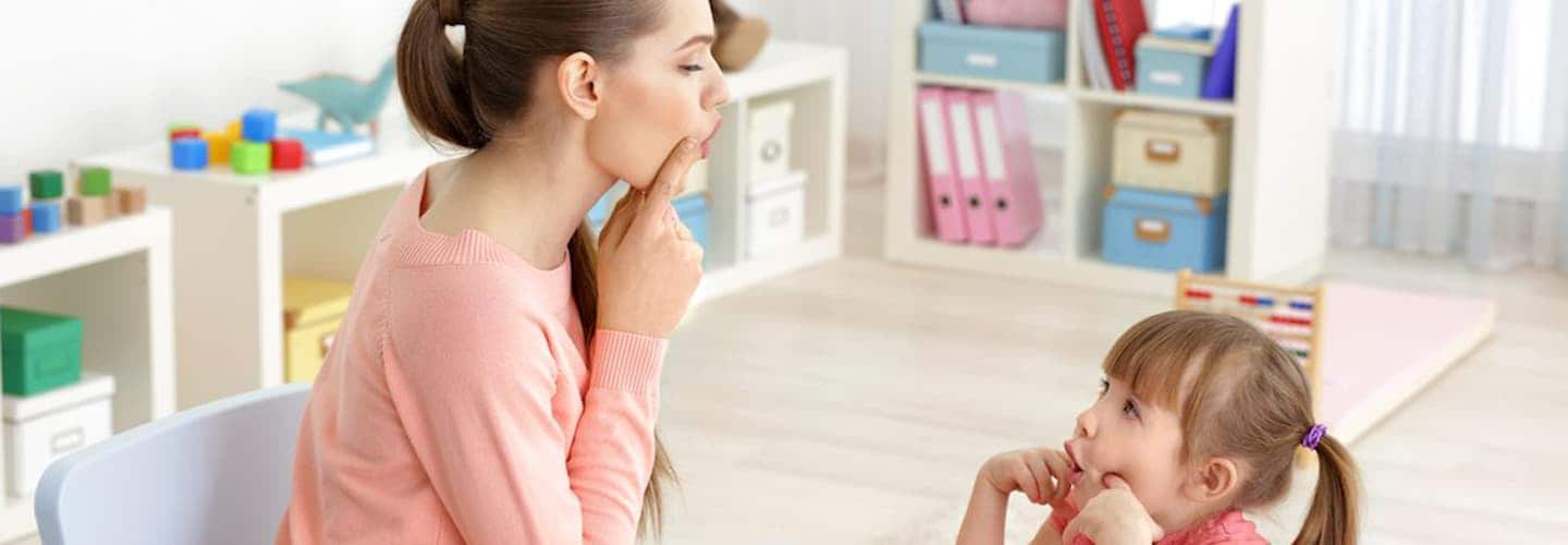 امرأة تشير إلى فمها في غرفة اللعب مع طفل ينسخ الإيماءة