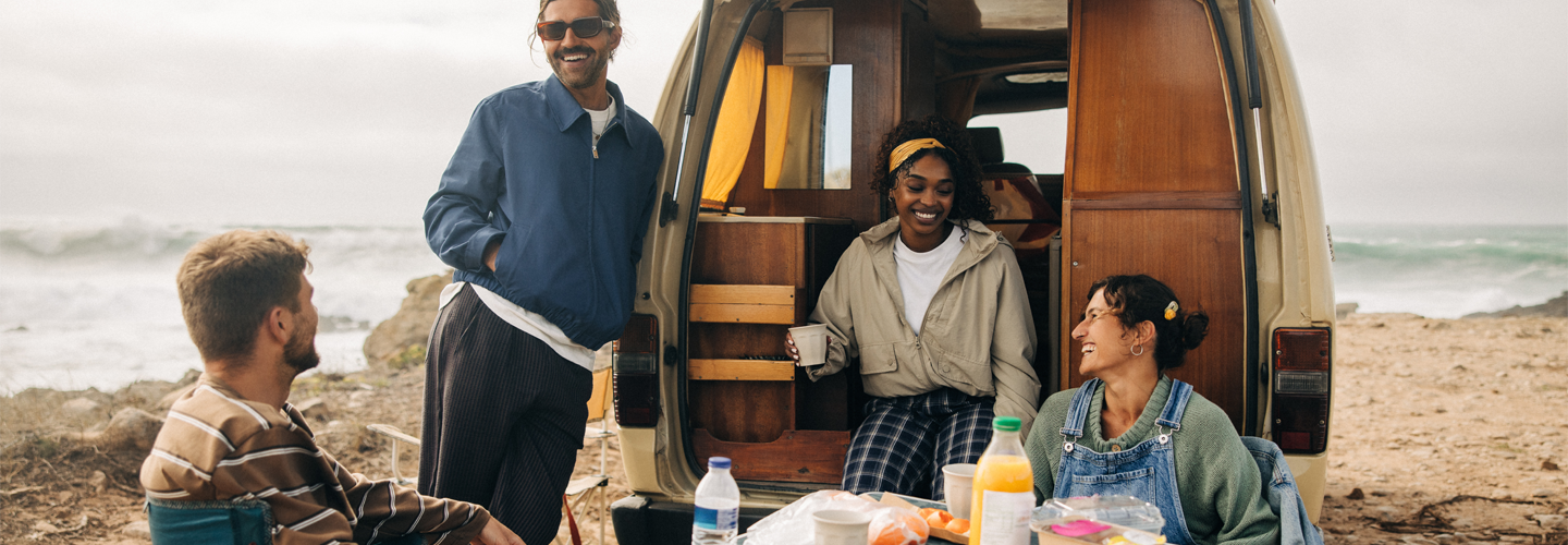Friends stood by a camper van with food by the sea socialising