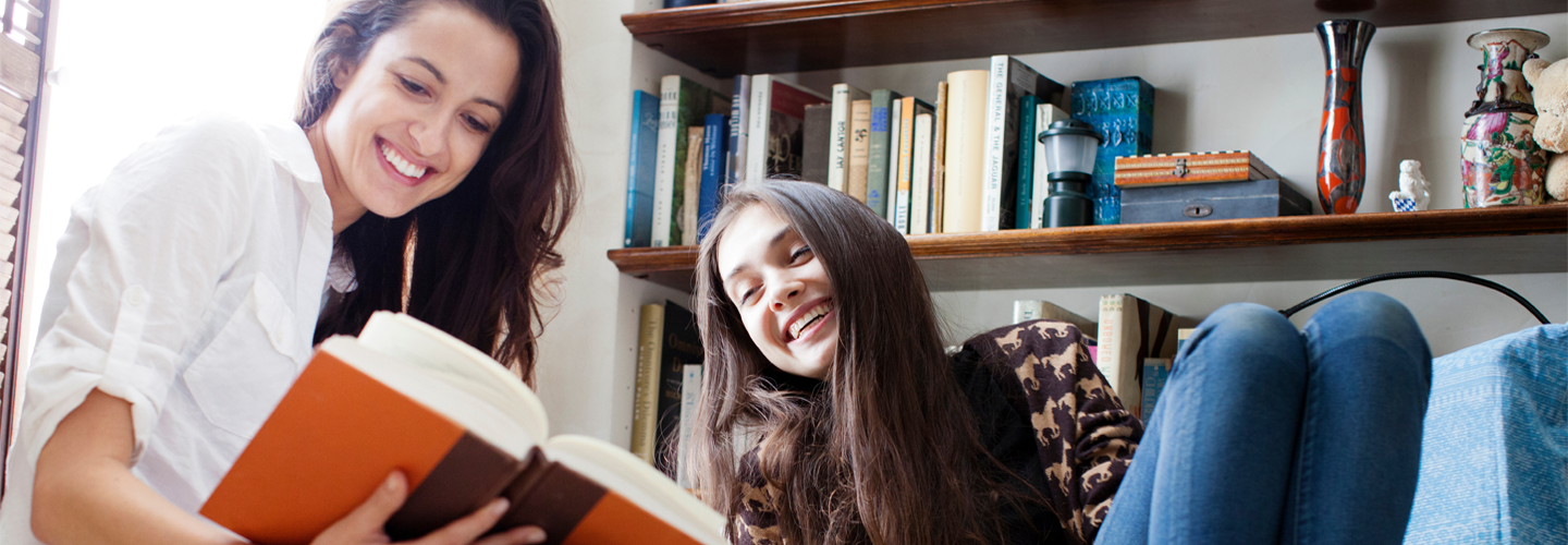 Two friends reading a book together smiling