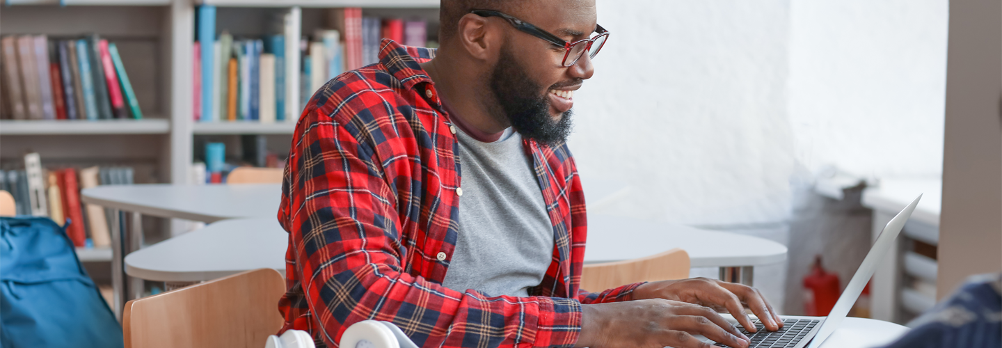 A man working on a laptop in a library smiling