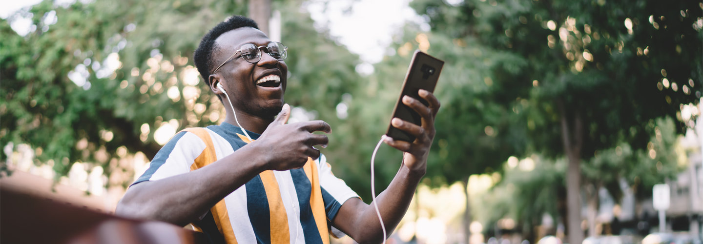 A man sat on a bench outdoors holding a phone smiling