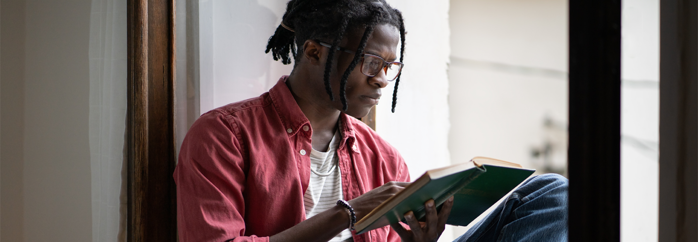 A man reading a book sat in a window