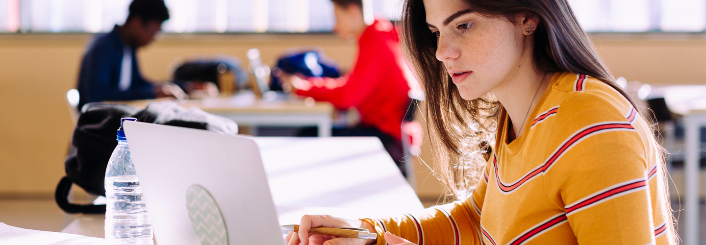 A young woman studying in a university library with a laptop