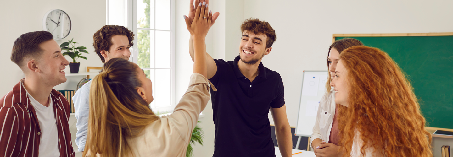 A group of students stood in a classroom high fiving eachother