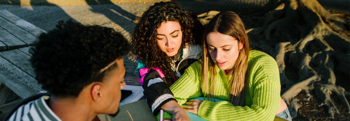 Students working outside at a wooden bench looking over papers